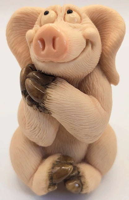 Piggin Romantic figurine by David Corbridge in 1997. A small sculpted pig figurine with a pink snout, beige skin, and dark brown claws, posed sitting with its paws over its mouth against a plain white background.
