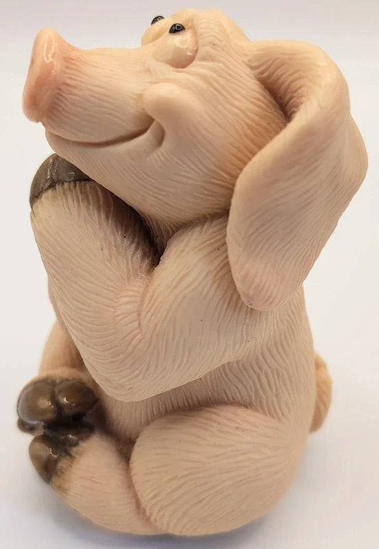 A small sculpted pig figurine sitting and holding its back legs, shown against a plain white background.