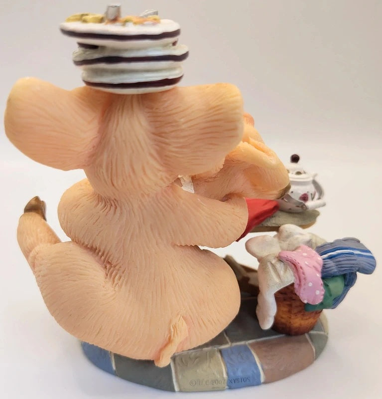 A vintage-style figurine of a pig character seen from behind, wearing a striped hat and carrying a basket with pink and blue items, set on a tiled base against a plain light background.