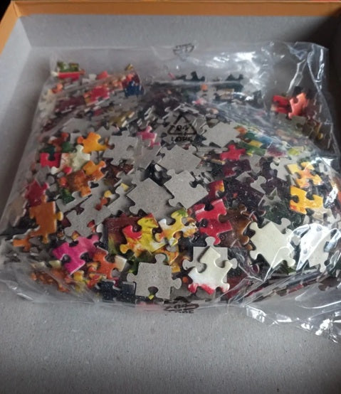 Jigsaw puzzle pieces in a clear plastic bag with a cardboard box lid.