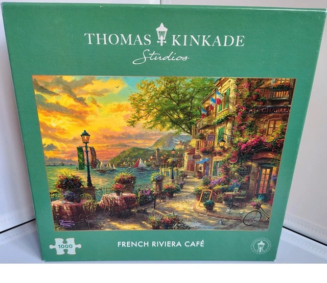 Jigsaw puzzle box featuring a Thomas Kinkade Studios painting of a French Riviera café.