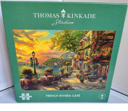 Jigsaw puzzle box featuring a Thomas Kinkade Studios painting of a French Riviera café.