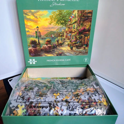 Jigsaw puzzle set with 'French Riviera Café' box by Thomas Kinkade Studios.