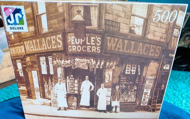 Jigsaw puzzle box featuring an old photograph of a store front with 'Wallaces' and 'People's Grocers' signs.