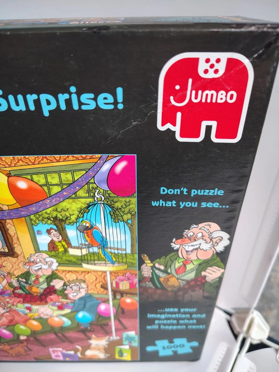 Jumbo brand jigsaw puzzle box featuring a black background, a red elephant logo, and a colorful illustration with the text 'Surprise!' and 'Don't puzzle what you see.