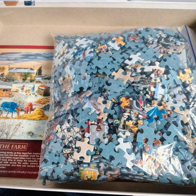 Jigsaw puzzle pieces in a clear bag with a partially completed puzzle and box in the background.